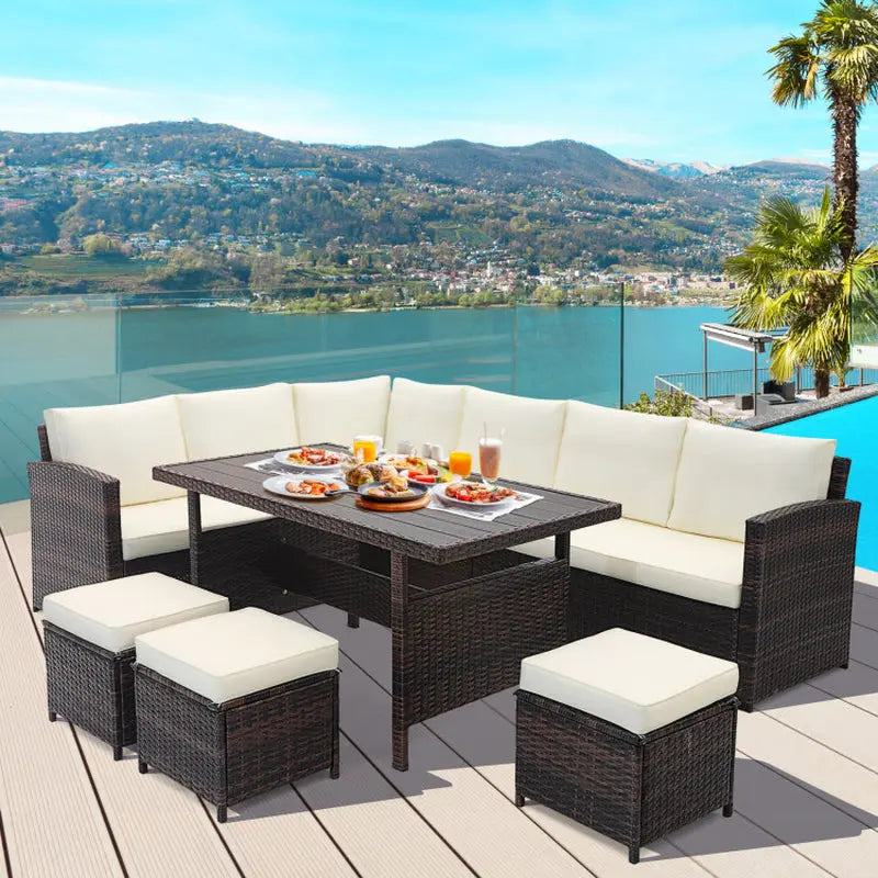 ELVORA Living 7-piece coastal dining set with cream cushions, wicker furniture on a deck by a pool and lake.